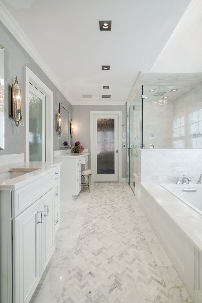 This is an example of a traditional ensuite bathroom in New York with white tiles, grey walls, marble flooring, marble worktops, recessed-panel cabinets, white cabinets, a built-in bath, a corner shower, a submerged sink and a hinged door.