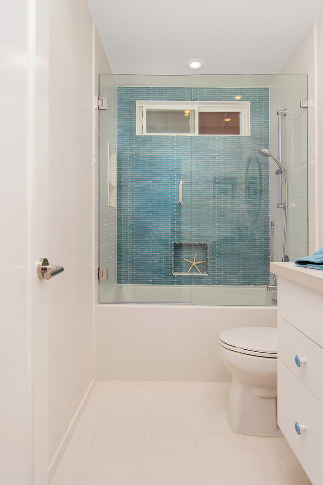 Cette photo montre une douche en alcôve moderne de taille moyenne pour enfant avec un placard à porte plane, des portes de placard blanches, une baignoire en alcôve, WC à poser, un carrelage bleu, un carrelage en pâte de verre, un mur blanc, un sol en carrelage de porcelaine, un lavabo encastré, un plan de toilette en quartz modifié, un sol blanc, une cabine de douche à porte battante et un plan de toilette gris.