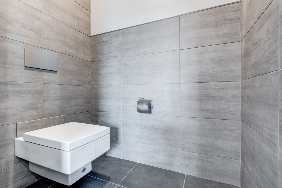 Cette image montre une grande salle de bain principale minimaliste avec un placard avec porte à panneau surélevé, des portes de placard blanches, une baignoire indépendante, une douche ouverte, WC suspendus, un carrelage gris, des carreaux de céramique, un mur gris, un sol en carrelage de céramique, un lavabo encastré, un plan de toilette en quartz, un sol gris et une cabine de douche à porte battante.