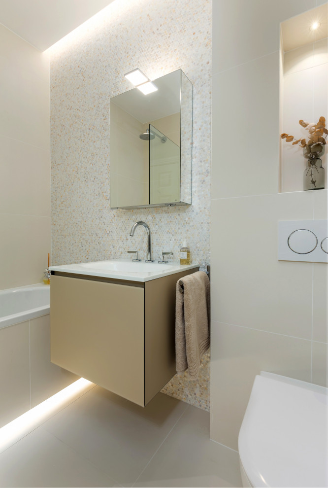 Modern inredning av ett litet vit vitt badrum, med luckor med glaspanel, beige skåp, ett platsbyggt badkar, en dusch/badkar-kombination, en vägghängd toalettstol, beige kakel, mosaik, beige väggar, klinkergolv i porslin, ett integrerad handfat, bänkskiva i glas, beiget golv och dusch med gångjärnsdörr