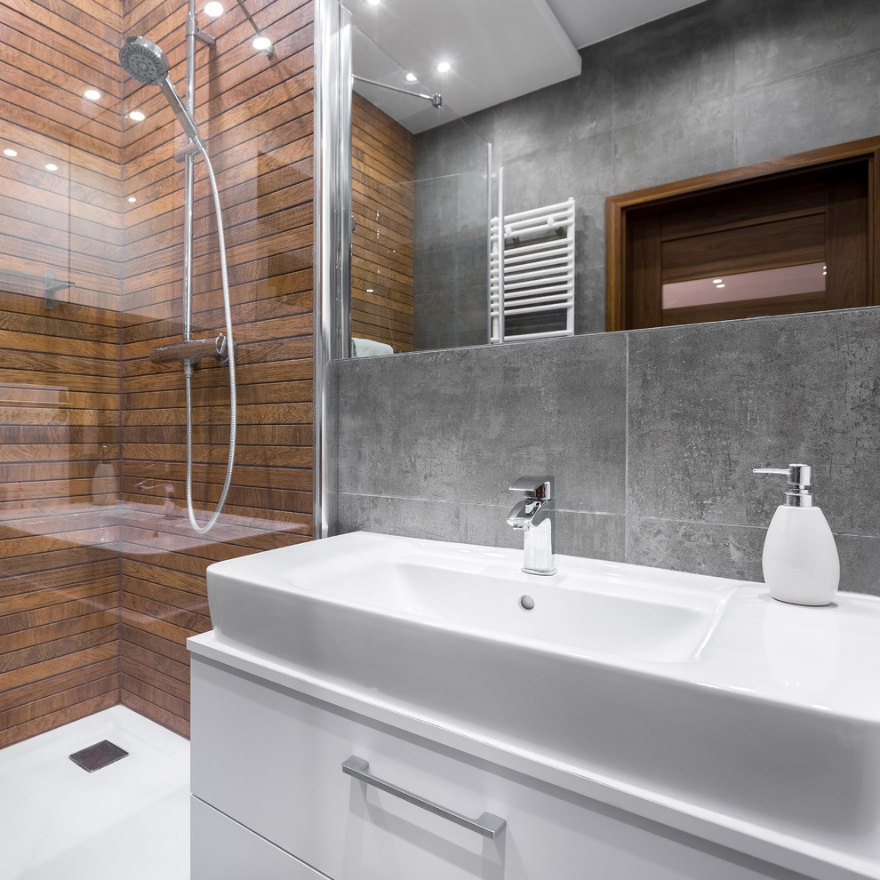 Inredning av ett modernt mellanstort vit vitt badrum, med släta luckor, vita skåp, en öppen dusch, grå kakel, stenkakel, grå väggar, ett nedsänkt handfat, bänkskiva i akrylsten och dusch med gångjärnsdörr