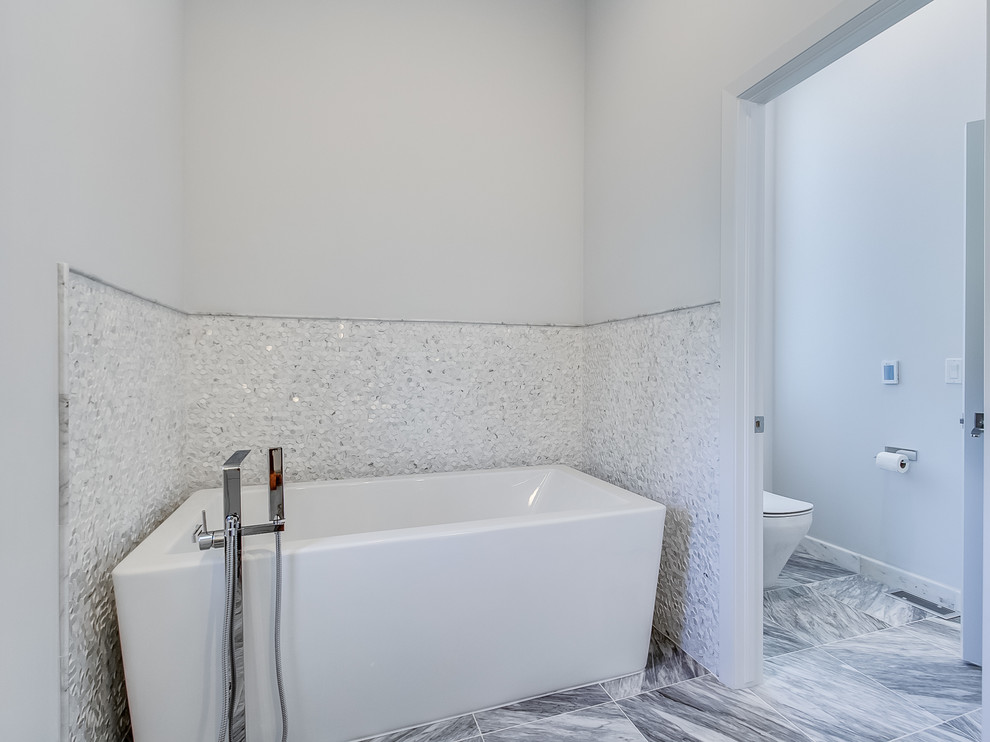 На фото: большая главная ванная комната в современном стиле с фасадами островного типа, серыми фасадами, отдельно стоящей ванной, серой плиткой, плиткой мозаикой, серыми стенами, мраморным полом, настольной раковиной и мраморной столешницей