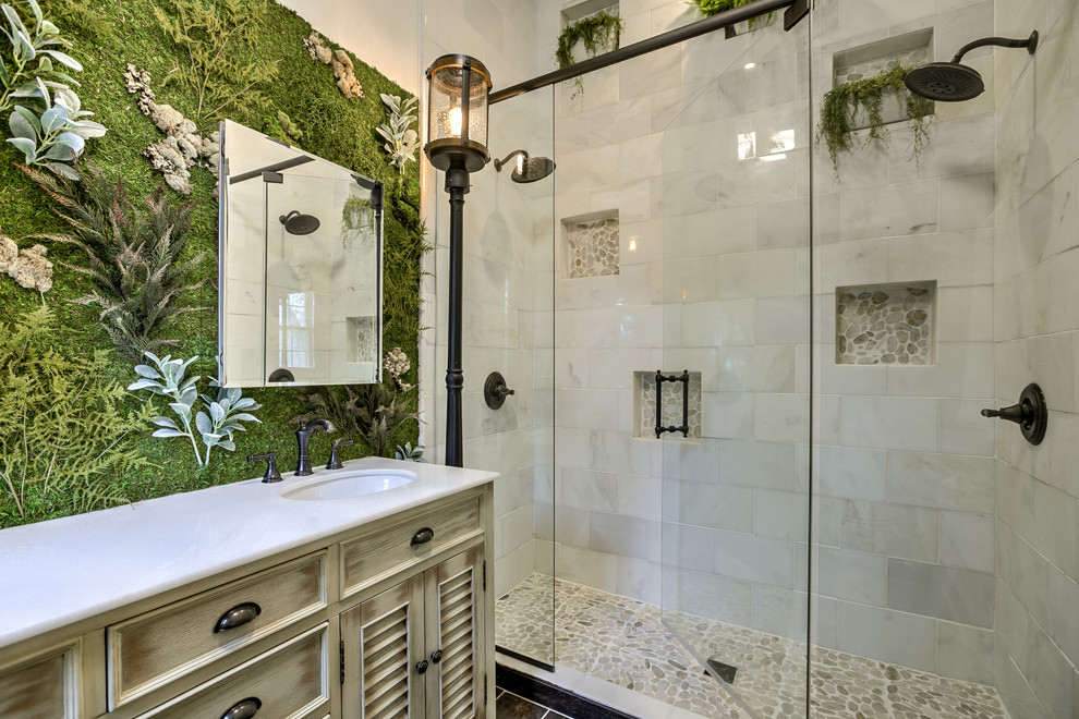 Пример оригинального дизайна: ванная комната в стиле кантри с фасадами с филенкой типа жалюзи, искусственно-состаренными фасадами, двойным душем, белой плиткой, врезной раковиной, душем с распашными дверями и белой столешницей