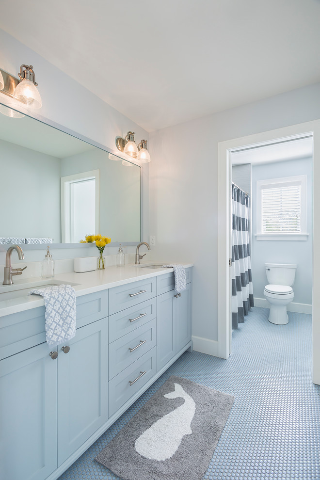 Cette image montre une salle de bain traditionnelle de taille moyenne pour enfant avec un placard à porte shaker, des portes de placard bleues, une baignoire en alcôve, un combiné douche/baignoire, WC à poser, des carreaux de céramique, un mur blanc, un sol en carrelage de céramique, un lavabo encastré, un plan de toilette en quartz modifié, un sol bleu, une cabine de douche avec un rideau et un plan de toilette blanc.