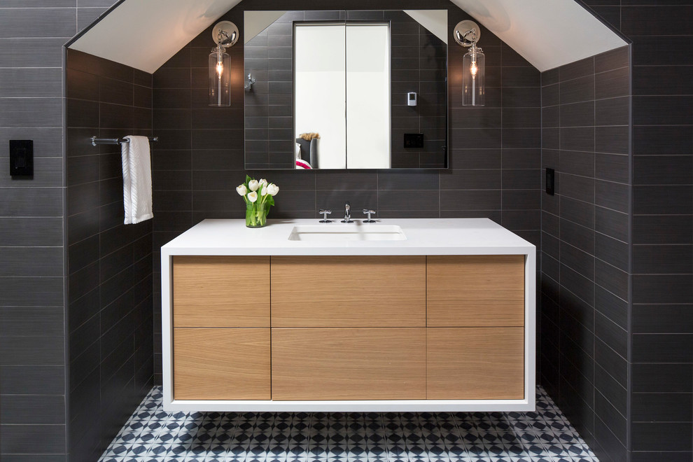 Réalisation d'une salle de bain design en bois clair avec un placard à porte plane, un carrelage noir, un lavabo encastré et un sol multicolore.
