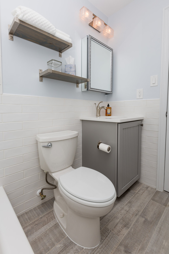 Lantlig inredning av ett mellanstort vit vitt badrum, med luckor med lamellpanel, grå skåp, ett badkar i en alkov, en dusch/badkar-kombination, en toalettstol med hel cisternkåpa, vit kakel, blå väggar, mörkt trägolv, ett undermonterad handfat, brunt golv och dusch med duschdraperi