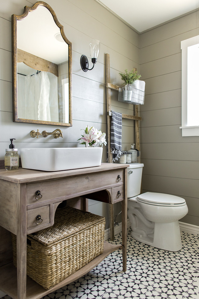 Claw-foot bathtub - small farmhouse master cement tile floor and black floor claw-foot bathtub idea in Tampa with furniture-like cabinets, light wood cabinets, a vessel sink, a two-piece toilet, gray walls and brown countertops