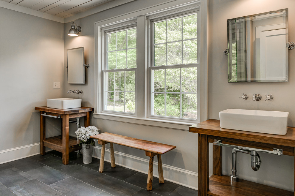 Lantlig inredning av ett badrum, med öppna hyllor, skåp i mellenmörkt trä, beige väggar, ett fristående handfat, träbänkskiva och grått golv