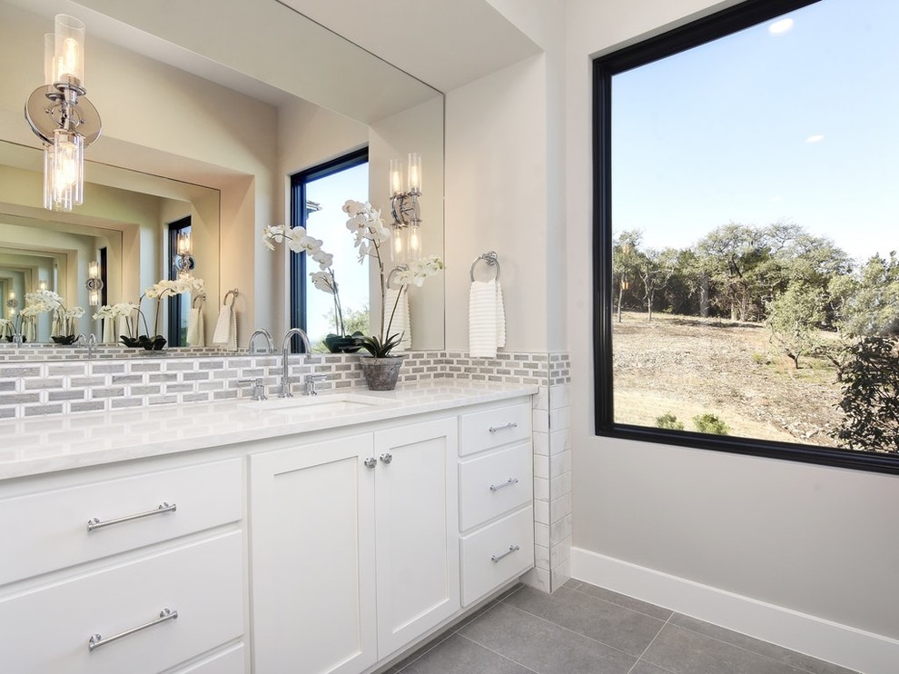This is an example of a large rural ensuite bathroom in Austin with shaker cabinets, white cabinets, a freestanding bath, an alcove shower, white tiles, metro tiles, grey walls, porcelain flooring, a submerged sink, solid surface worktops, grey floors, a hinged door and white worktops.