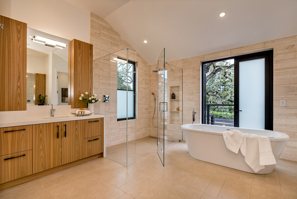 Стильный дизайн: ванная комната в современном стиле с врезной раковиной, плоскими фасадами, отдельно стоящей ванной, угловым душем, бежевой плиткой, каменной плиткой, бежевыми стенами, полом из травертина и фасадами цвета дерева среднего тона - последний тренд