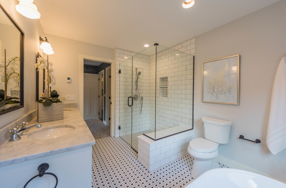 Idéer för mellanstora lantliga vitt en-suite badrum, med skåp i shakerstil, vita skåp, ett fristående badkar, en kantlös dusch, en toalettstol med hel cisternkåpa, grå kakel, tunnelbanekakel, grå väggar, klinkergolv i keramik, ett undermonterad handfat, marmorbänkskiva, flerfärgat golv och dusch med gångjärnsdörr