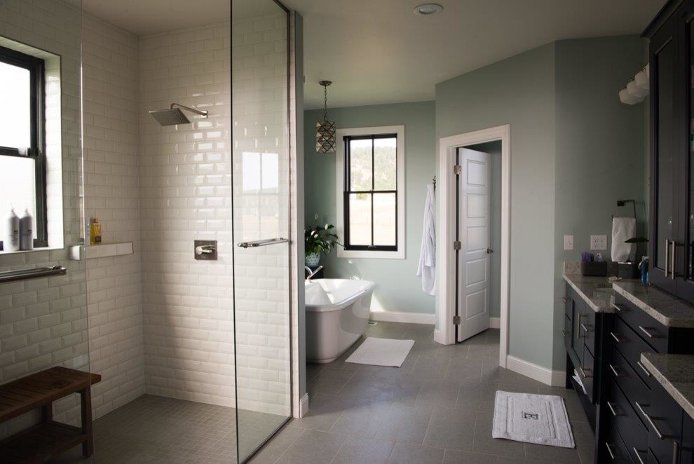 This is an example of a medium sized farmhouse ensuite bathroom in Other with recessed-panel cabinets, black cabinets, a freestanding bath, a walk-in shower, white tiles, metro tiles, grey walls, porcelain flooring, a submerged sink, granite worktops, grey floors and a shower curtain.