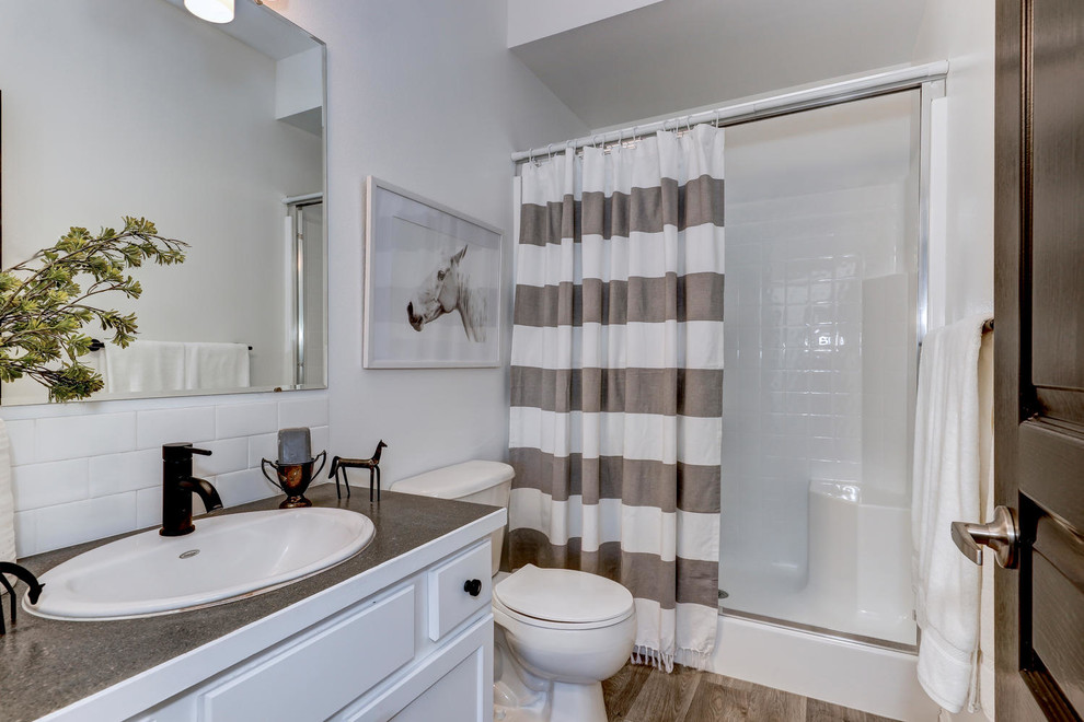 Photo of a medium sized farmhouse bathroom in Boise with shaker cabinets, white cabinets, an alcove shower, white tiles, ceramic tiles, white walls, laminate floors, laminate worktops, a sliding door and grey worktops.