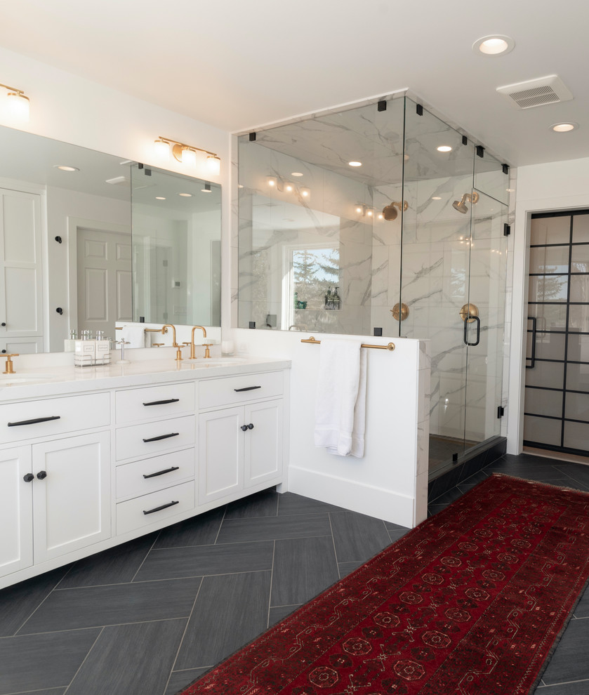 Пример оригинального дизайна: большая главная ванная комната в стиле кантри с фасадами в стиле шейкер, белыми фасадами, отдельно стоящей ванной, душем над ванной, раздельным унитазом, белой плиткой, керамогранитной плиткой, белыми стенами, полом из сланца, врезной раковиной, столешницей из искусственного кварца, черным полом, душем с распашными дверями и белой столешницей