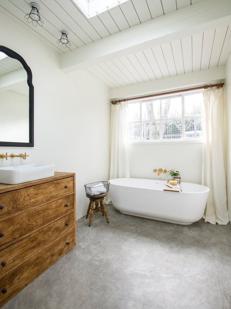 Lantlig inredning av ett en-suite badrum, med skåp i mellenmörkt trä, ett fristående badkar, vita väggar, betonggolv, ett fristående handfat, grått golv och släta luckor