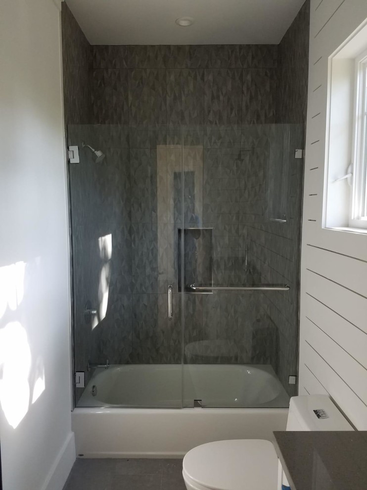 Exempel på ett mellanstort lantligt grå grått badrum med dusch, med skåp i shakerstil, vita skåp, ett badkar i en alkov, en dusch/badkar-kombination, en toalettstol med hel cisternkåpa, grå kakel, porslinskakel, vita väggar, klinkergolv i porslin, ett undermonterad handfat, bänkskiva i akrylsten, grått golv och dusch med skjutdörr