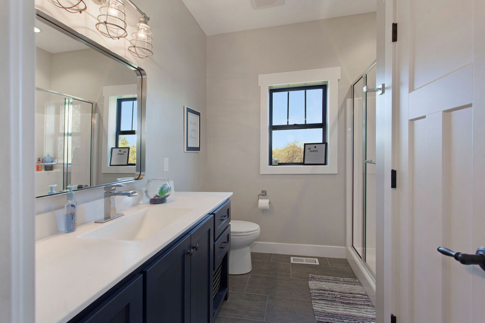 Bild på ett mellanstort lantligt vit vitt badrum med dusch, med skåp i shakerstil, blå skåp, en dusch i en alkov, en toalettstol med separat cisternkåpa, grå väggar, klinkergolv i porslin, ett integrerad handfat, bänkskiva i akrylsten, grått golv och dusch med gångjärnsdörr