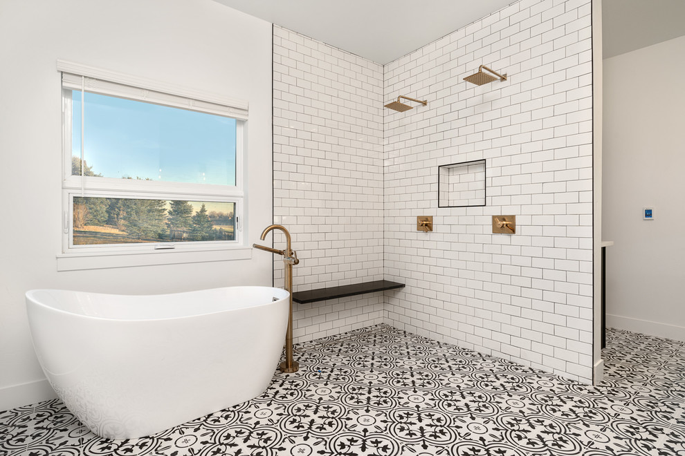 Diseño de cuarto de baño principal de estilo de casa de campo grande con armarios estilo shaker, puertas de armario negras, bañera exenta, ducha a ras de suelo, sanitario de dos piezas, baldosas y/o azulejos blancos, baldosas y/o azulejos de cerámica, paredes blancas, suelo de azulejos de cemento, lavabo bajoencimera, encimera de cuarzo compacto, suelo multicolor, ducha abierta y encimeras blancas