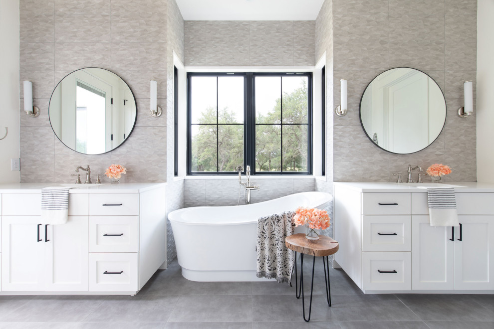 На фото: ванная комната в стиле кантри с фасадами в стиле шейкер, белыми фасадами, отдельно стоящей ванной, серой плиткой, врезной раковиной, серым полом и белой столешницей с