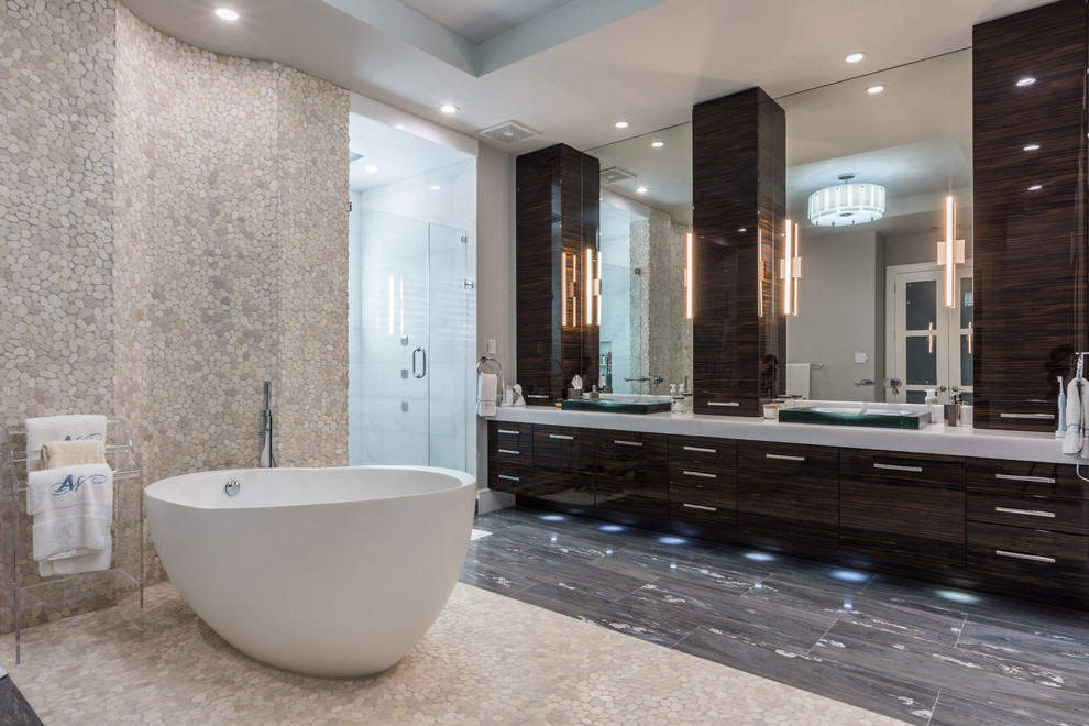 This is an example of a large modern ensuite bathroom in Miami with flat-panel cabinets, dark wood cabinets, a freestanding bath, a double shower, grey tiles, marble tiles, a vessel sink, marble worktops, beige walls, ceramic flooring, grey floors and a hinged door.