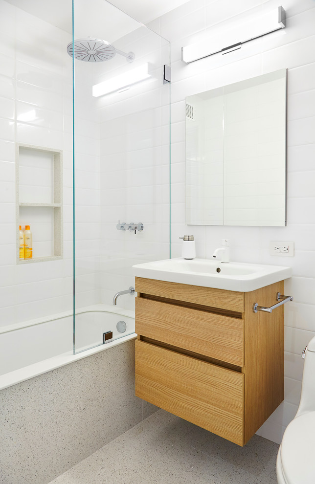 Réalisation d'une petite salle de bain minimaliste en bois clair avec un placard à porte plane, un combiné douche/baignoire, WC à poser, un carrelage blanc, des carreaux de céramique, un mur blanc, sol en béton ciré, un lavabo suspendu et une baignoire encastrée.