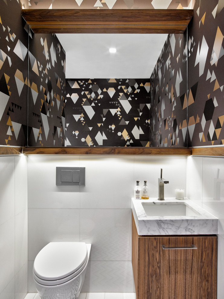 Cette photo montre une petite salle de bain tendance en bois brun avec un placard à porte plane, WC à poser, un carrelage blanc, un carrelage en pâte de verre, un mur multicolore, un sol en marbre, un lavabo encastré et un plan de toilette en marbre.