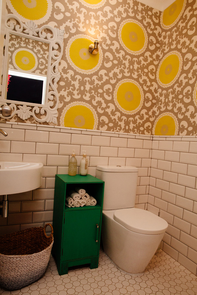 Modern inredning av ett litet badrum, med möbel-liknande, gröna skåp, en vägghängd toalettstol, vit kakel, keramikplattor, flerfärgade väggar, klinkergolv i keramik och ett väggmonterat handfat