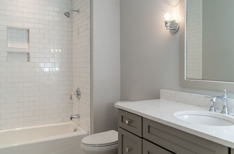 Idée de décoration pour une petite salle de bain avec un placard à porte shaker, des portes de placard grises, une baignoire en alcôve, un combiné douche/baignoire, WC à poser, un carrelage gris, des carreaux de céramique, un mur gris, un sol en carrelage de porcelaine, un lavabo encastré, un plan de toilette en quartz modifié, un sol gris, une cabine de douche avec un rideau, un plan de toilette blanc, meuble simple vasque et meuble-lavabo encastré.