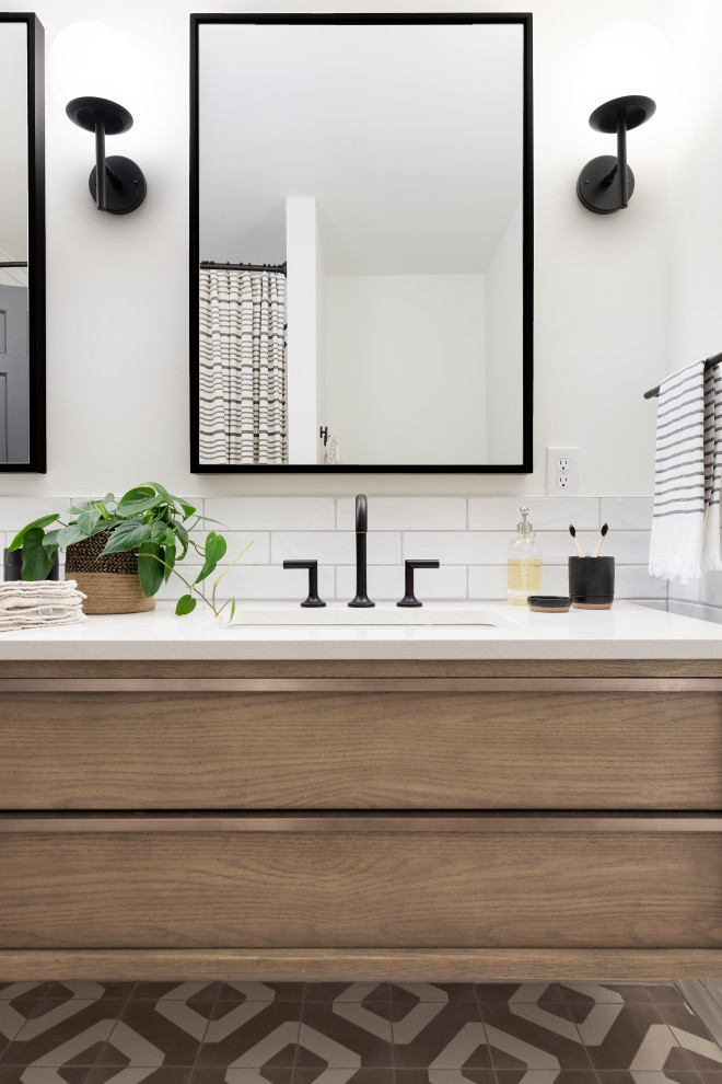 Design ideas for a classic family bathroom in Minneapolis with flat-panel cabinets, medium wood cabinets, an alcove bath, a shower/bath combination, white tiles, ceramic tiles, porcelain flooring, a submerged sink, engineered stone worktops, multi-coloured floors, a shower curtain and white worktops.