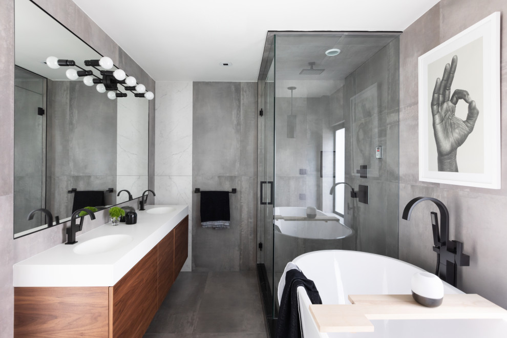 Imagen de cuarto de baño doble y flotante contemporáneo con bañera exenta, paredes grises, suelo gris, encimeras blancas, armarios con paneles lisos, puertas de armario de madera en tonos medios, ducha esquinera, baldosas y/o azulejos grises y lavabo integrado