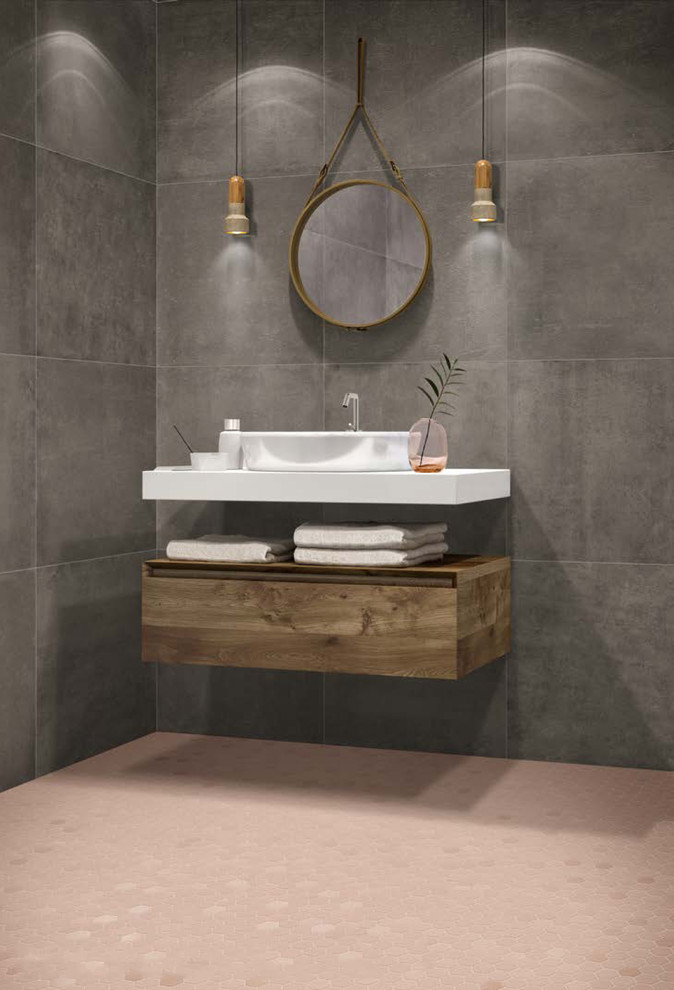 Cette image montre une salle d'eau minimaliste en bois brun avec un placard à porte plane, un carrelage gris, des carreaux de porcelaine, un mur gris, un sol en carrelage de porcelaine, un plan de toilette blanc, une vasque et un sol rose.