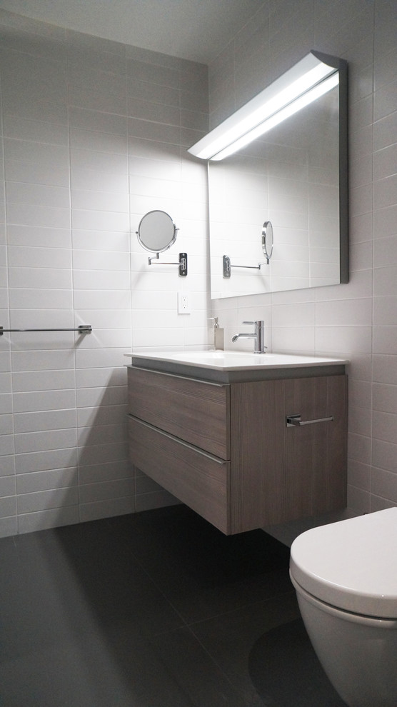 Idéer för att renovera ett mellanstort funkis vit vitt badrum med dusch, med släta luckor, skåp i ljust trä, vit kakel, keramikplattor, vita väggar, klinkergolv i porslin, ett integrerad handfat, en vägghängd toalettstol, svart golv och bänkskiva i akrylsten
