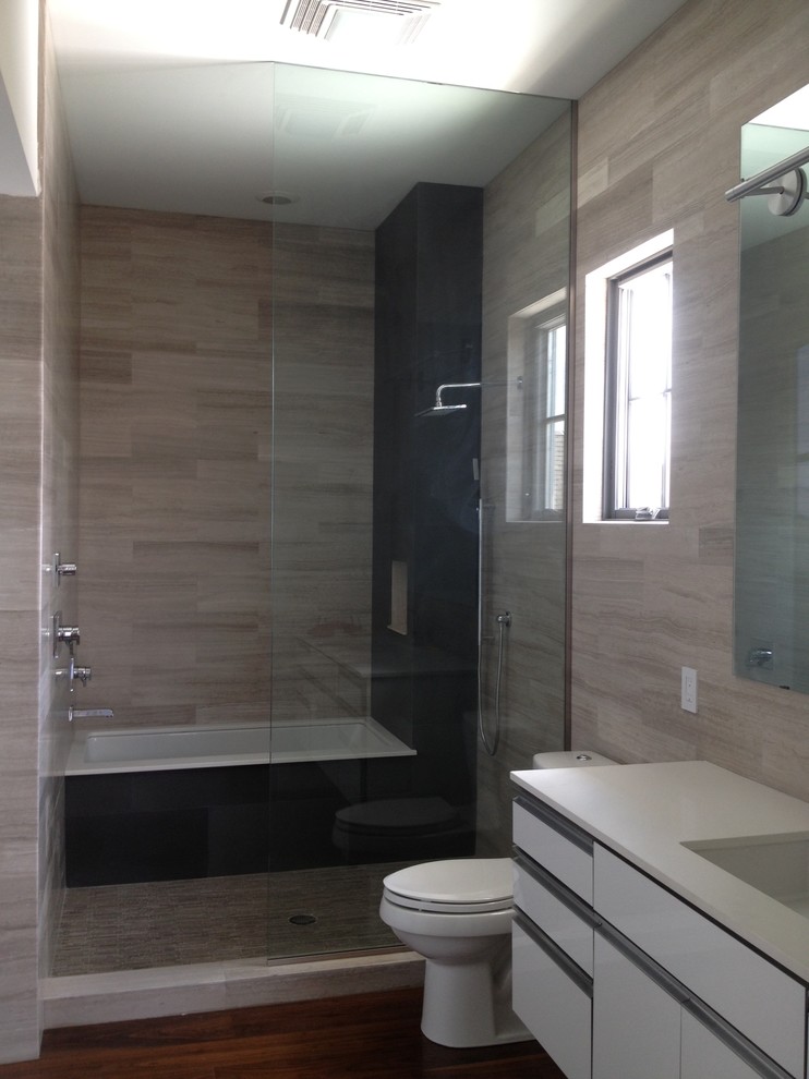 Inredning av ett modernt stort vit vitt badrum med dusch, med släta luckor, vita skåp, ett undermonterat badkar, våtrum, en toalettstol med hel cisternkåpa, grå kakel, porslinskakel, mellanmörkt trägolv, ett undermonterad handfat, bänkskiva i kvarts, brunt golv och med dusch som är öppen