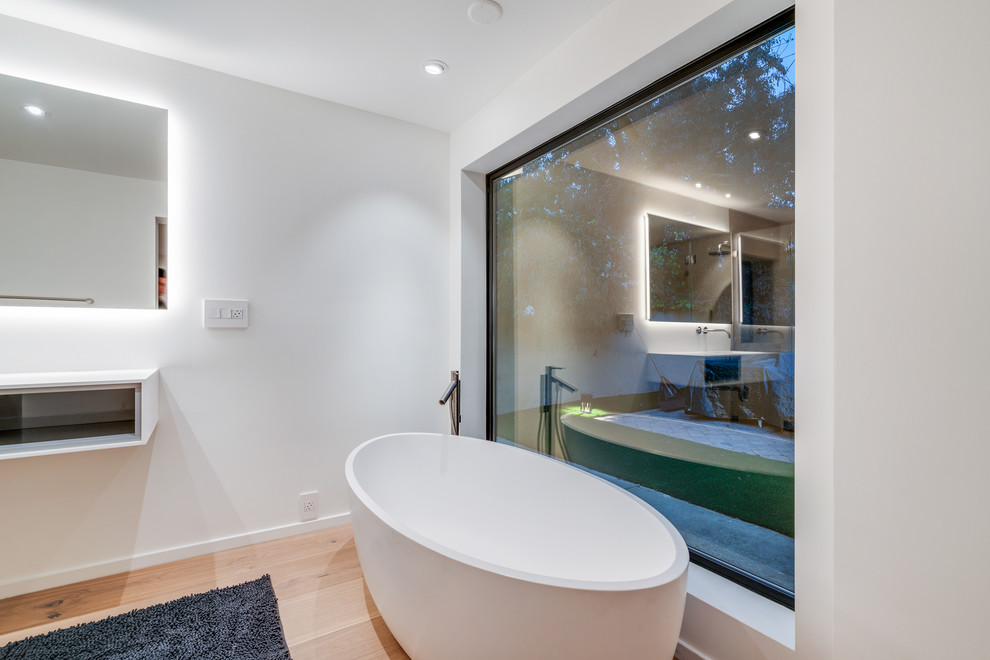 Inspiration for a medium sized modern ensuite bathroom in San Francisco with flat-panel cabinets, white cabinets, a freestanding bath, a built-in shower, a one-piece toilet, beige tiles, porcelain tiles, white walls, light hardwood flooring, an integrated sink, engineered stone worktops, beige floors, a hinged door and white worktops.