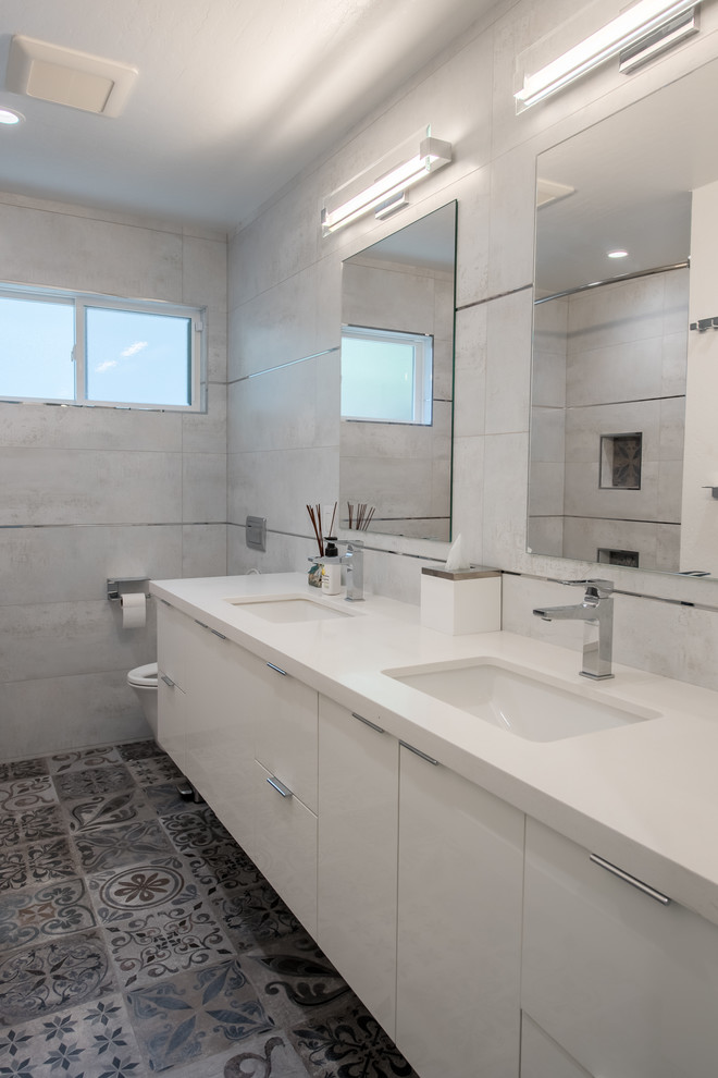 Modern inredning av ett mellanstort vit vitt badrum för barn, med släta luckor, ett platsbyggt badkar, en kantlös dusch, en bidé, beige kakel, keramikplattor, beige väggar, ett undermonterad handfat, grått golv, dusch med duschdraperi, vita skåp, cementgolv och bänkskiva i akrylsten