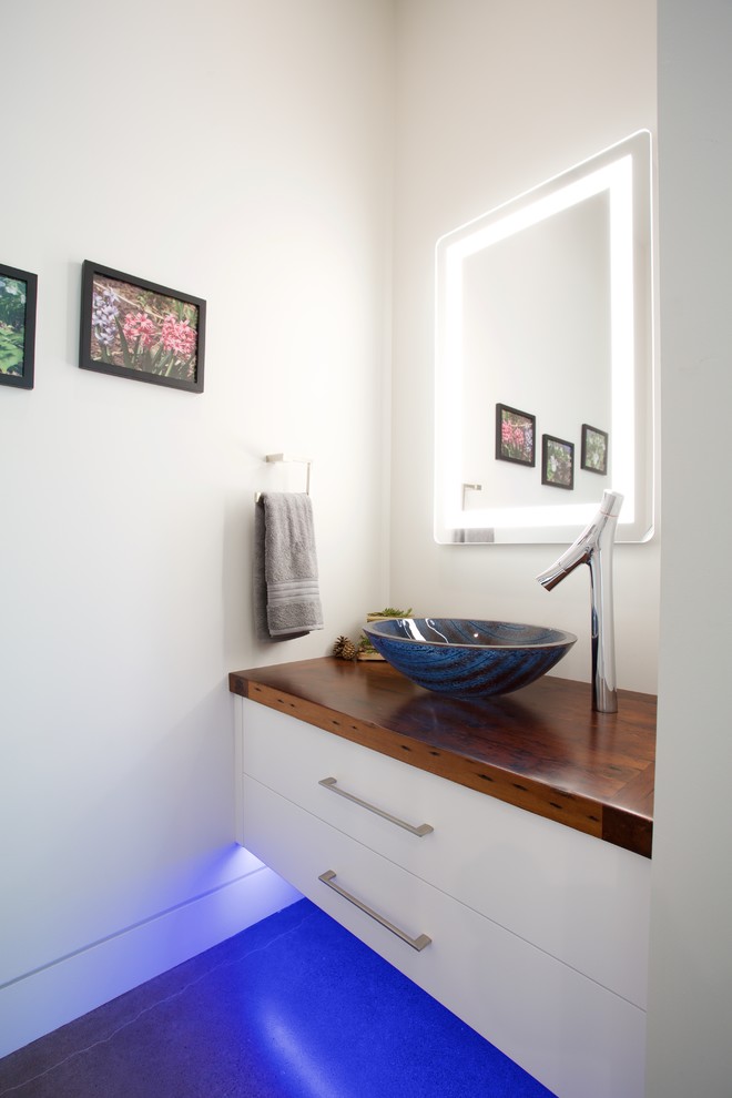 Modelo de cuarto de baño actual pequeño con armarios con paneles lisos, puertas de armario blancas, baldosas y/o azulejos multicolor, paredes beige, suelo de cemento, lavabo sobreencimera y encimera de madera
