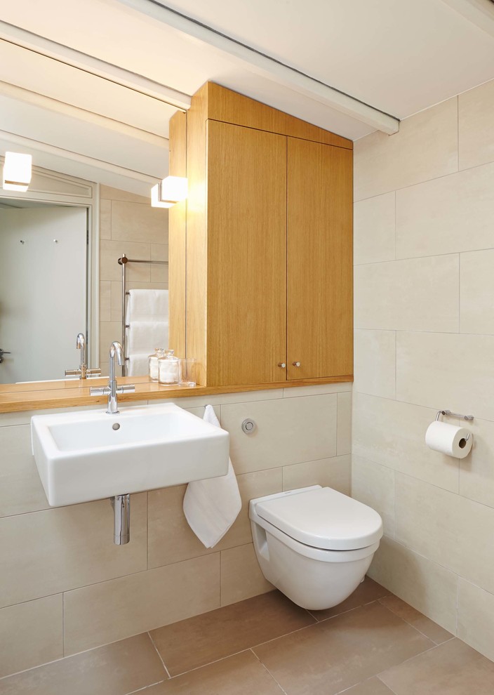 Design ideas for a medium sized contemporary ensuite bathroom in Hampshire with a wall-mounted sink, flat-panel cabinets, light wood cabinets, wooden worktops, an alcove shower, a wall mounted toilet, beige tiles, porcelain tiles, beige walls and porcelain flooring.