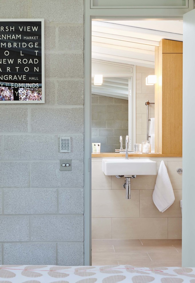 Inredning av ett modernt mellanstort en-suite badrum, med ett väggmonterat handfat, släta luckor, skåp i ljust trä, träbänkskiva, beige kakel, porslinskakel, beige väggar, klinkergolv i porslin, en dusch i en alkov och en vägghängd toalettstol