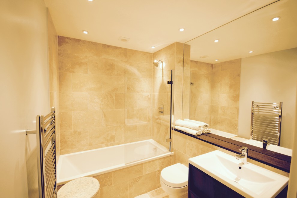 Medium sized contemporary family bathroom in London with a built-in sink, dark wood cabinets, wooden worktops, a built-in bath, a built-in shower, a two-piece toilet, beige tiles, stone tiles, beige walls and limestone flooring.