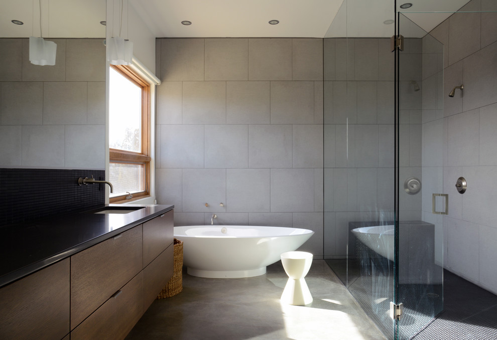 Bathroom - modern gray tile and ceramic tile concrete floor and gray floor bathroom idea in Albuquerque with flat-panel cabinets, medium tone wood cabinets, gray walls, an undermount sink, granite countertops and a hinged shower door