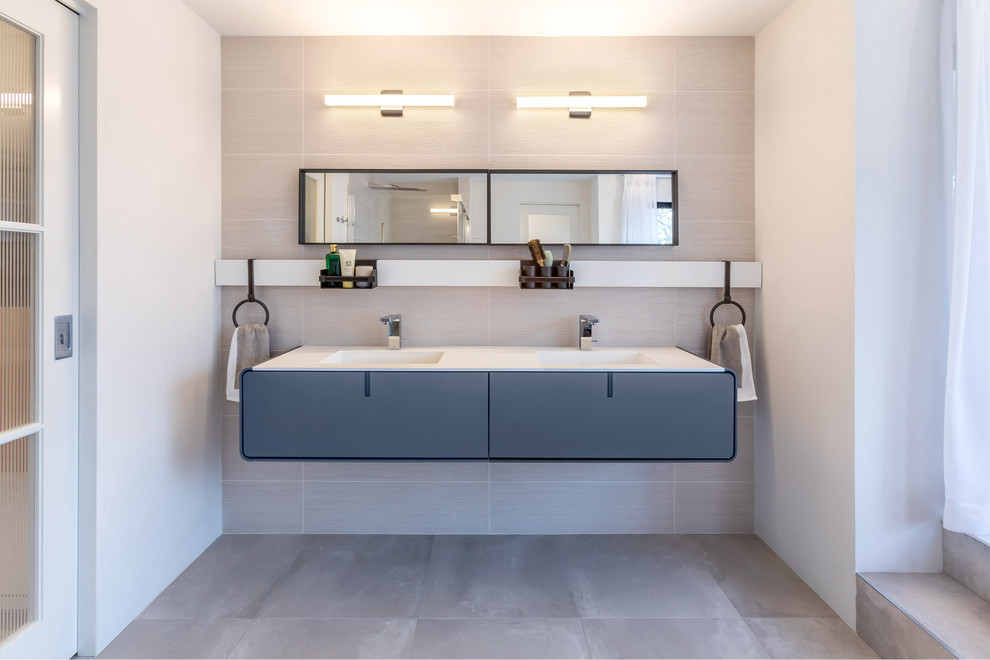 Пример оригинального дизайна: главная ванная комната в современном стиле с плоскими фасадами, керамогранитной плиткой, белыми стенами, полом из керамогранита, монолитной раковиной, столешницей из искусственного камня, серым полом, белой столешницей, серыми фасадами, серой плиткой и зеркалом с подсветкой