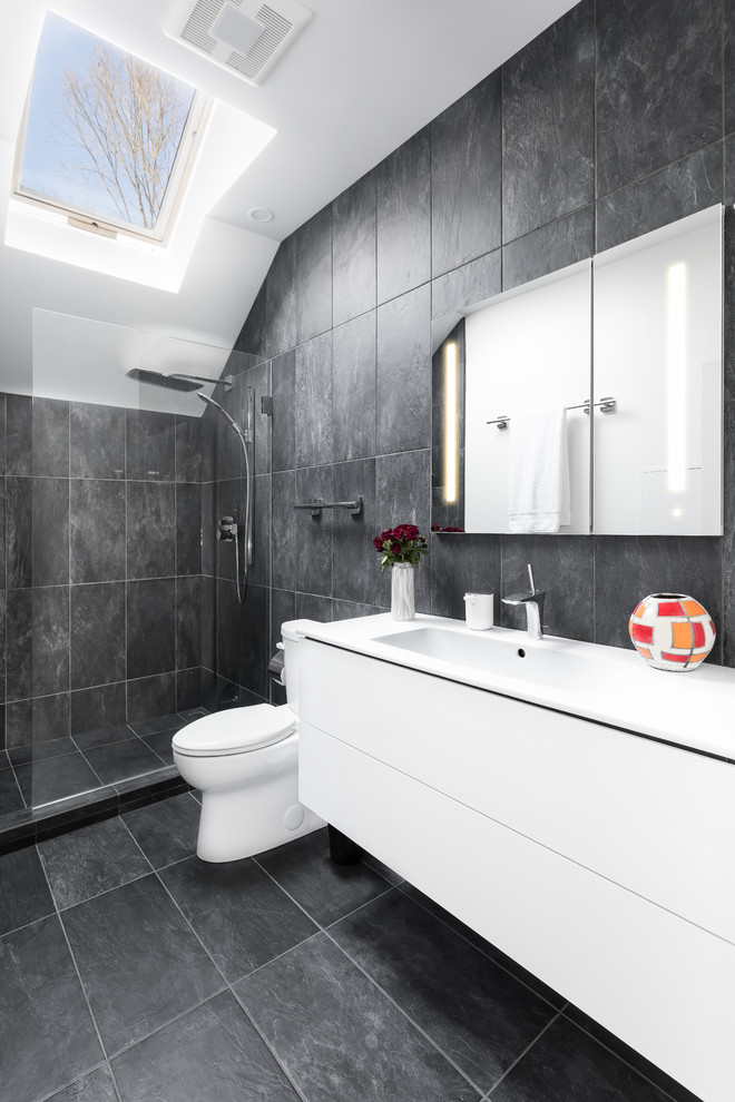 Example of a mid-sized minimalist master black tile and porcelain tile porcelain tile and black floor walk-in shower design in Boston with flat-panel cabinets, white cabinets, a one-piece toilet, black walls, an integrated sink, quartz countertops, a hinged shower door and white countertops