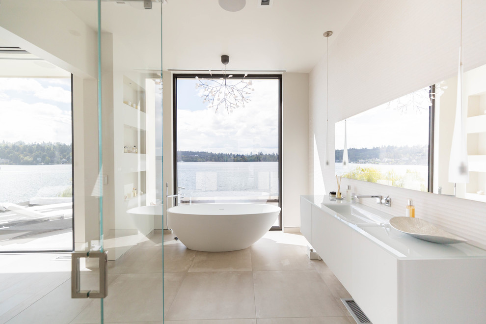 Cette photo montre une salle de bain tendance avec un placard à porte plane, des portes de placard blanches, une baignoire indépendante, un mur blanc, une vasque, un sol beige et un plan de toilette blanc.