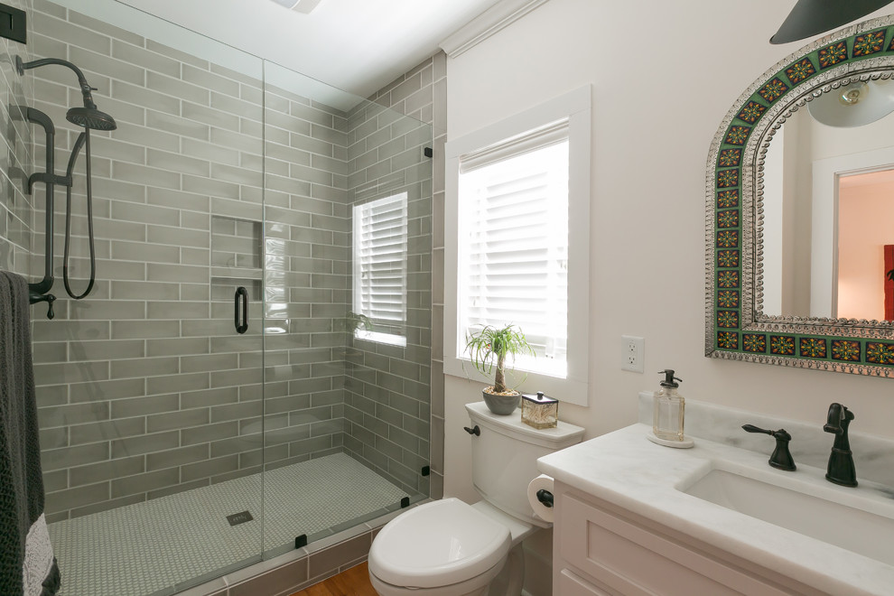 Пример оригинального дизайна: детская ванная комната среднего размера в стиле неоклассика (современная классика) с фасадами с утопленной филенкой, душем в нише, унитазом-моноблоком, керамической плиткой, белыми стенами, темным паркетным полом, врезной раковиной, столешницей из гранита, коричневым полом, душем с распашными дверями, белой столешницей и серой плиткой