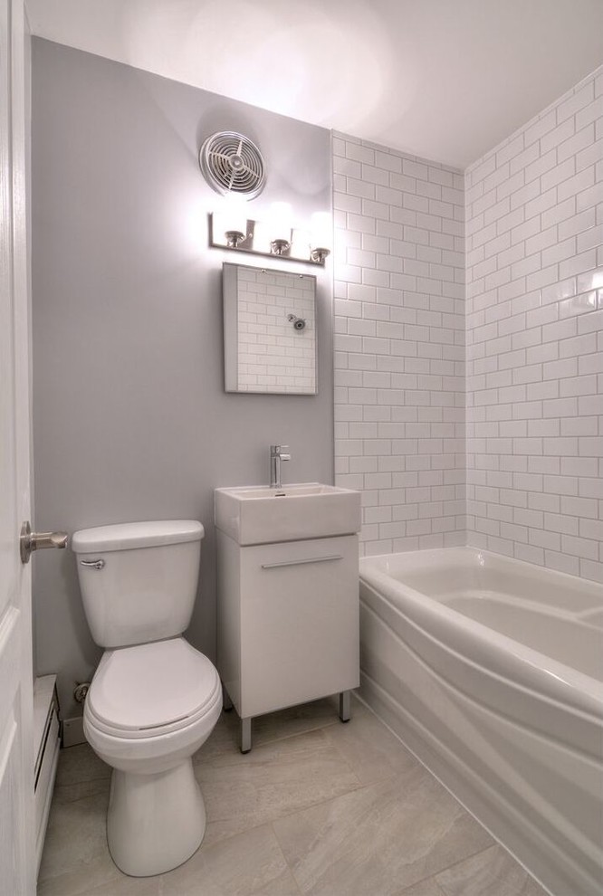 Cette image montre une petite salle d'eau traditionnelle avec un placard à porte plane, des portes de placard blanches, une baignoire en alcôve, un combiné douche/baignoire, WC séparés, un carrelage blanc, un carrelage métro, un mur gris, un sol en carrelage de porcelaine, une vasque, un sol beige et une cabine de douche avec un rideau.