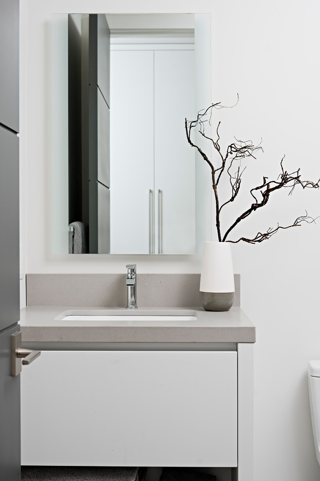 Modern inredning av ett mellanstort grå grått badrum, med släta luckor, vita skåp, en kantlös dusch, en vägghängd toalettstol, grå kakel, porslinskakel, vita väggar, ljust trägolv, ett undermonterad handfat och bänkskiva i kvarts