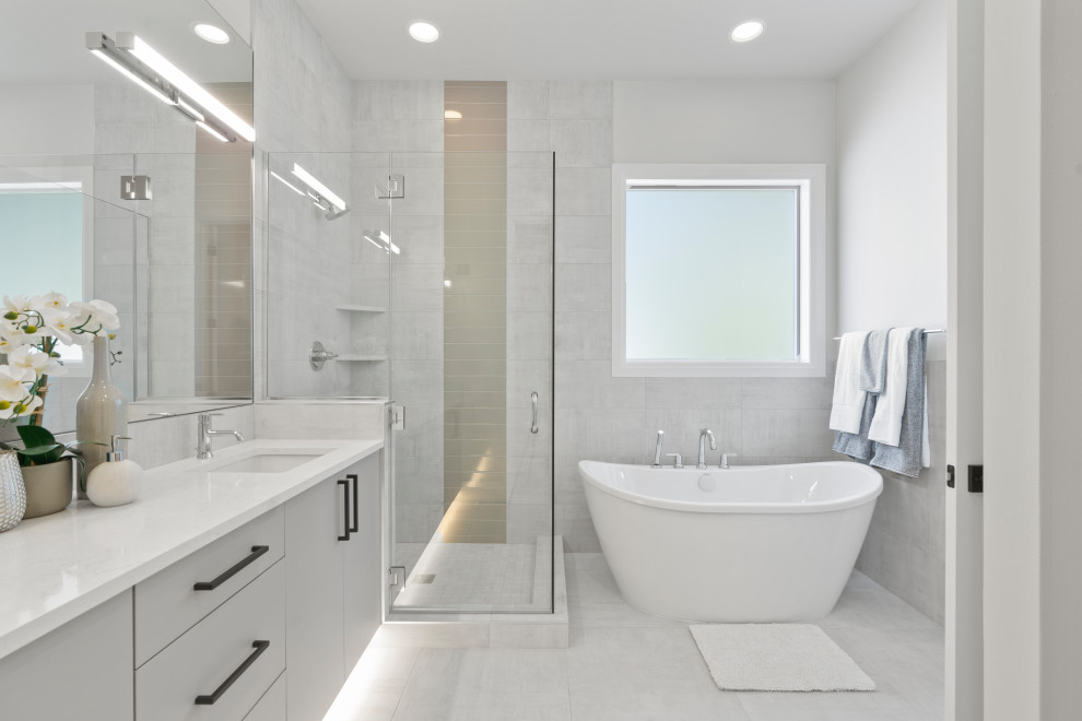 Bild på ett funkis vit vitt badrum, med släta luckor, grå skåp, ett fristående badkar, grå kakel, vita väggar, ett undermonterad handfat och grått golv