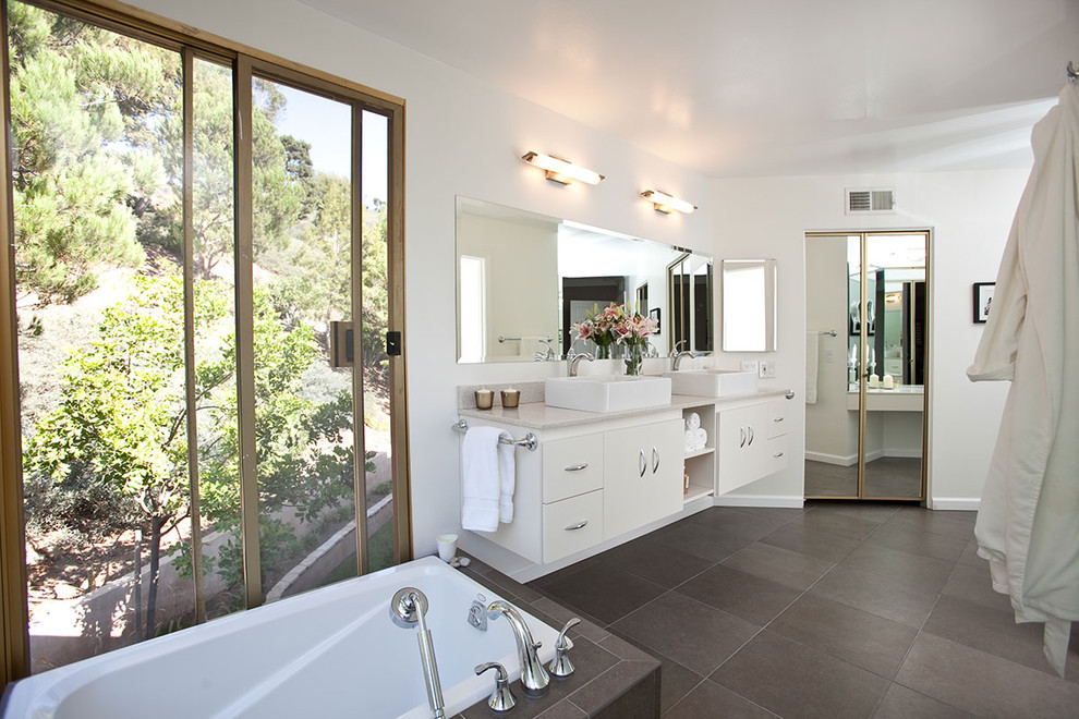 Идея дизайна: ванная комната в стиле модернизм с настольной раковиной, плоскими фасадами, белыми фасадами, угловой ванной, белыми стенами, полом из керамогранита и серой плиткой
