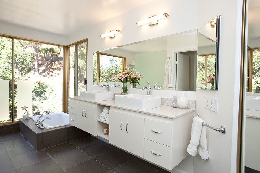 Foto på ett mycket stort funkis badrum, med ett fristående handfat, släta luckor, vita skåp, vita väggar, klinkergolv i porslin, grå kakel och ett platsbyggt badkar
