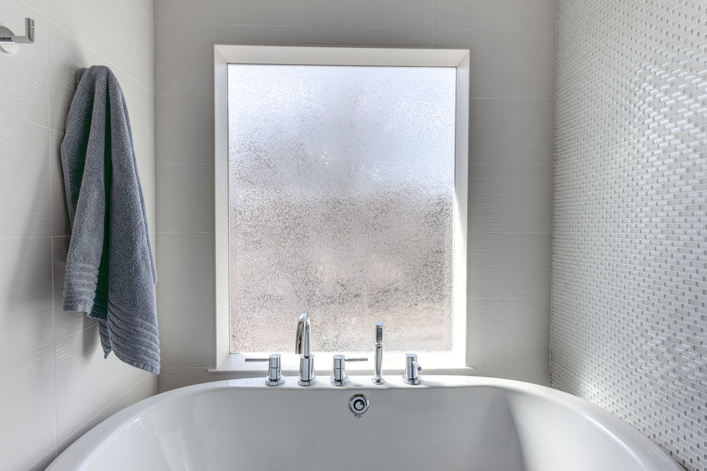 This is an example of a large modern ensuite bathroom in Minneapolis with a trough sink, flat-panel cabinets, dark wood cabinets, engineered stone worktops, a freestanding bath, a double shower, a two-piece toilet, white tiles, glass tiles, grey walls and ceramic flooring.